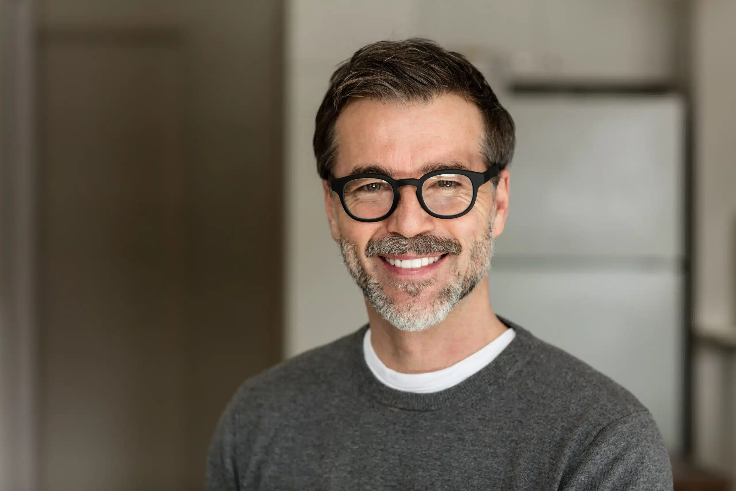 Smiling middle-aged man wearing glasses and a gray sweater, representing a confident and approachable individual