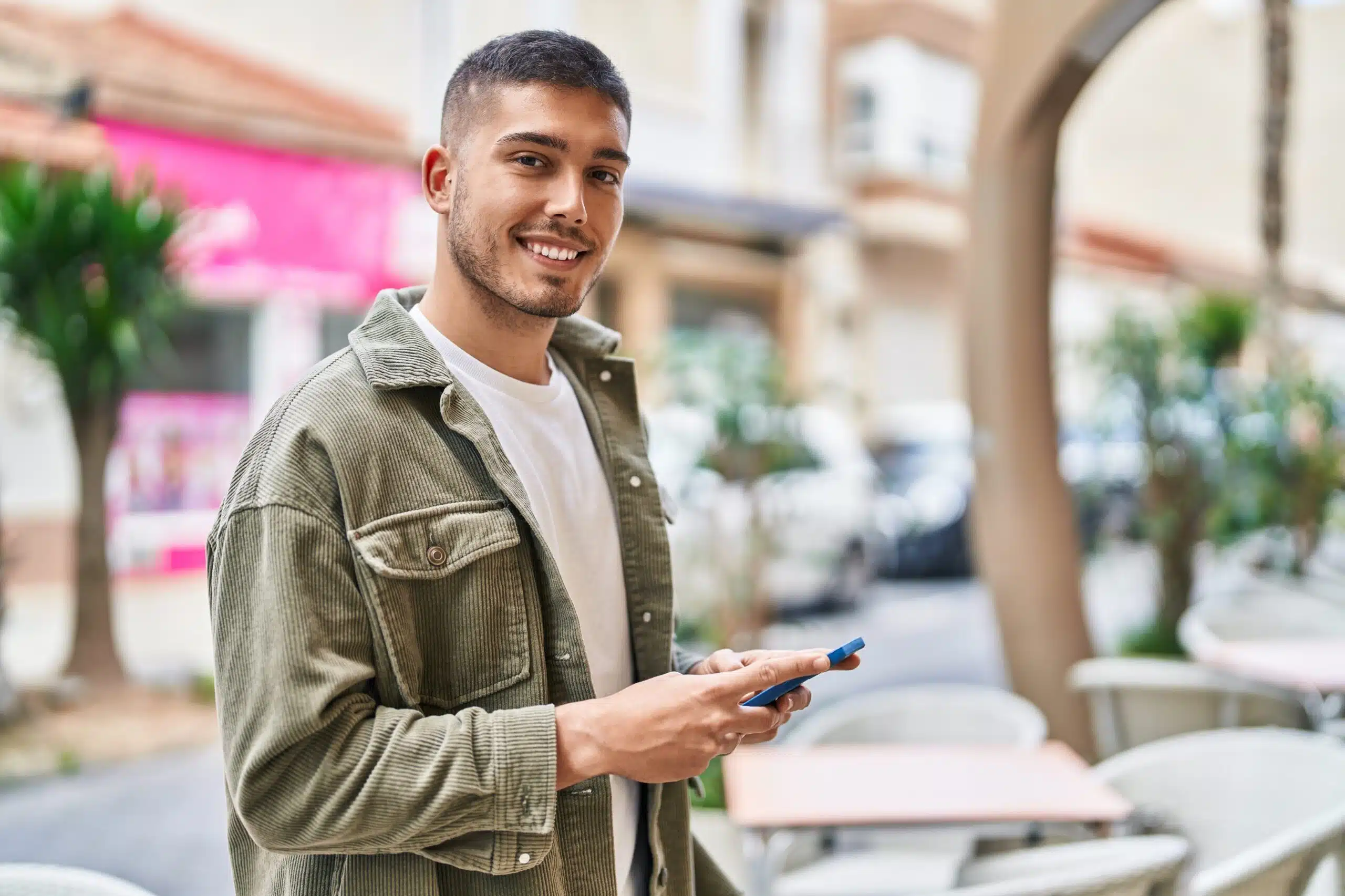 Smiling man in a green jacket holding a smartphone outdoors