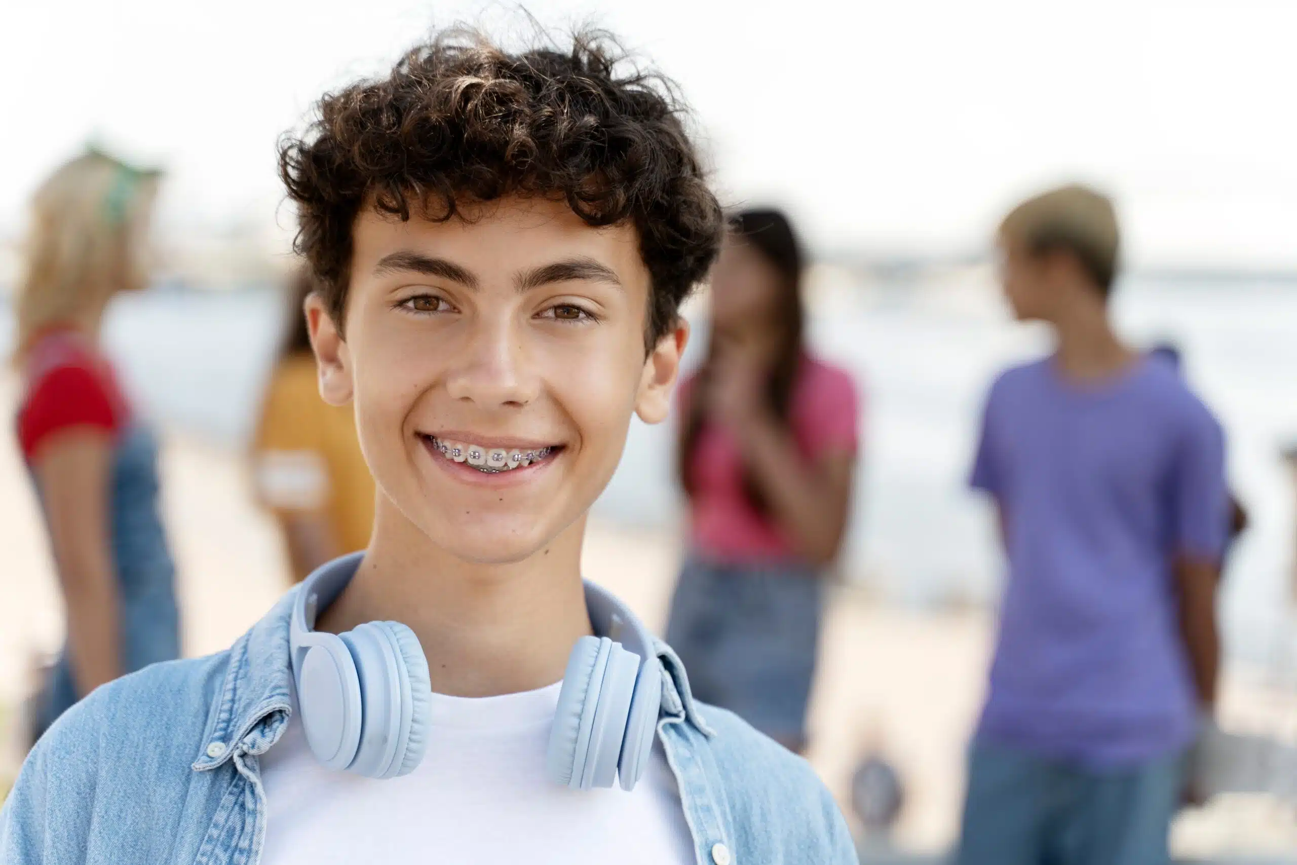Smiling teenage boy wearing headphones with other teenagers in the background