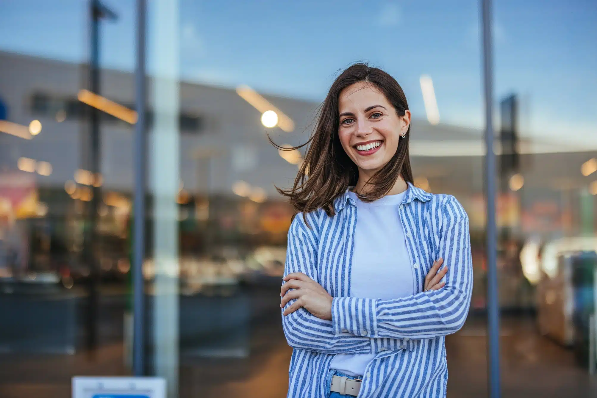 Smiling woman standing with arms crossed outdoors in front of a modern building