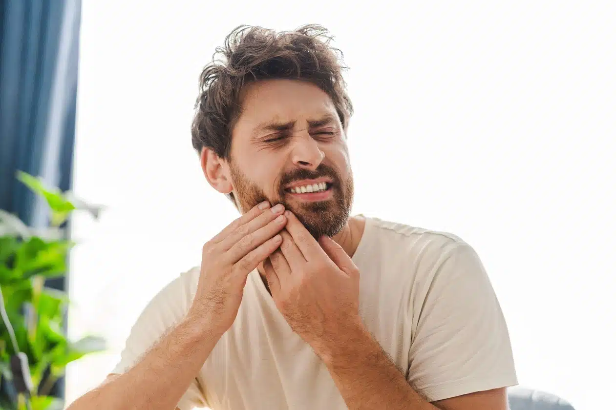 Man experiencing tooth pain while touching his jaw