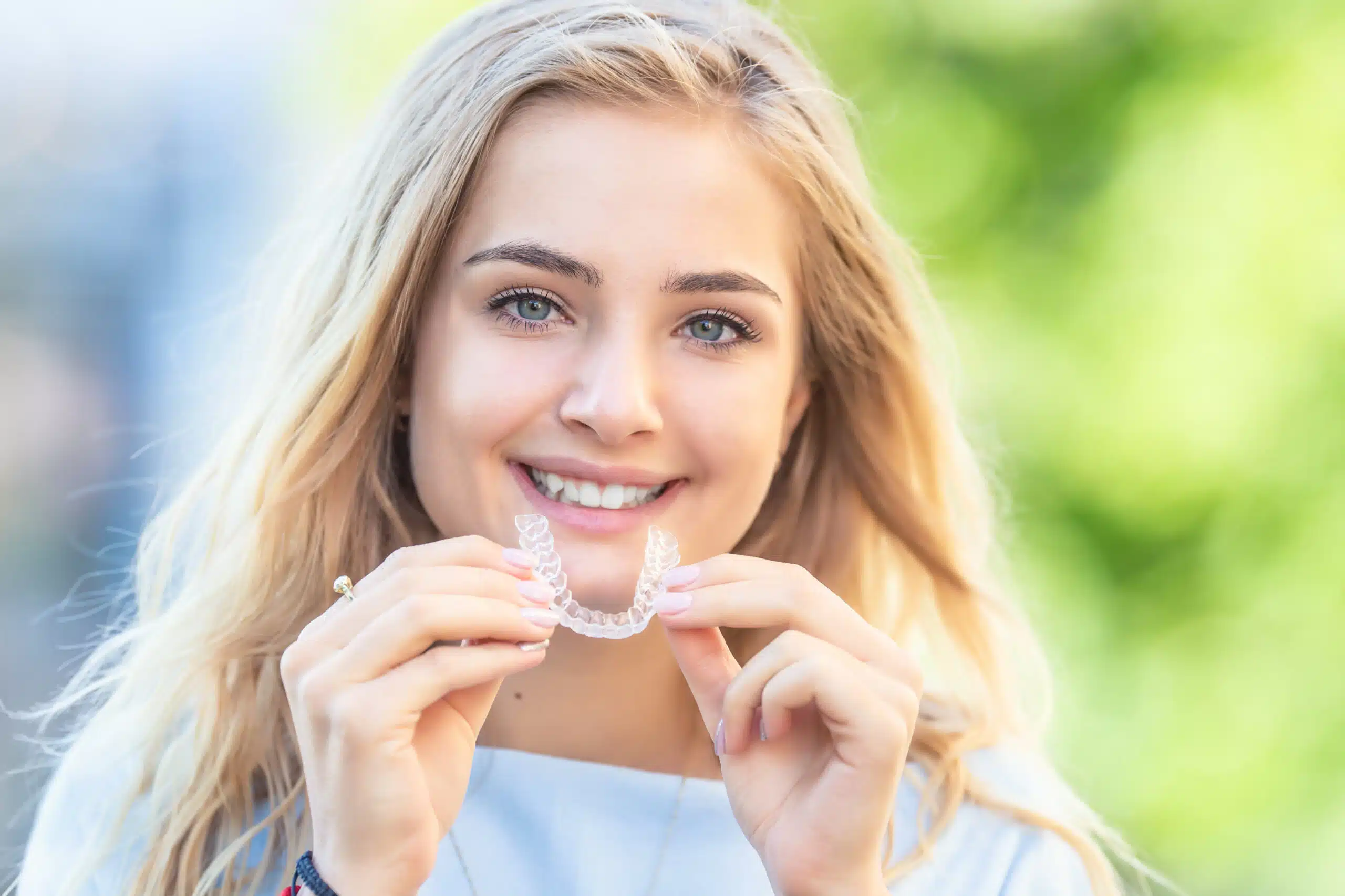 Smiling woman holding a clear dental aligner